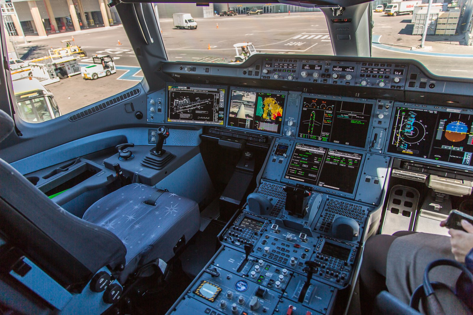 Wide view across an Airbus A350 flight deck with the airport visible through the windows